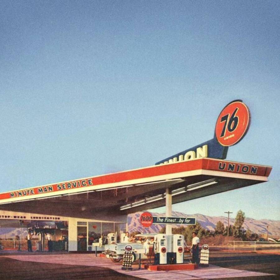A vintage Union 76 gas station with red, white, and blue signage, cars at the pumps, and mountains in the background on a clear day.