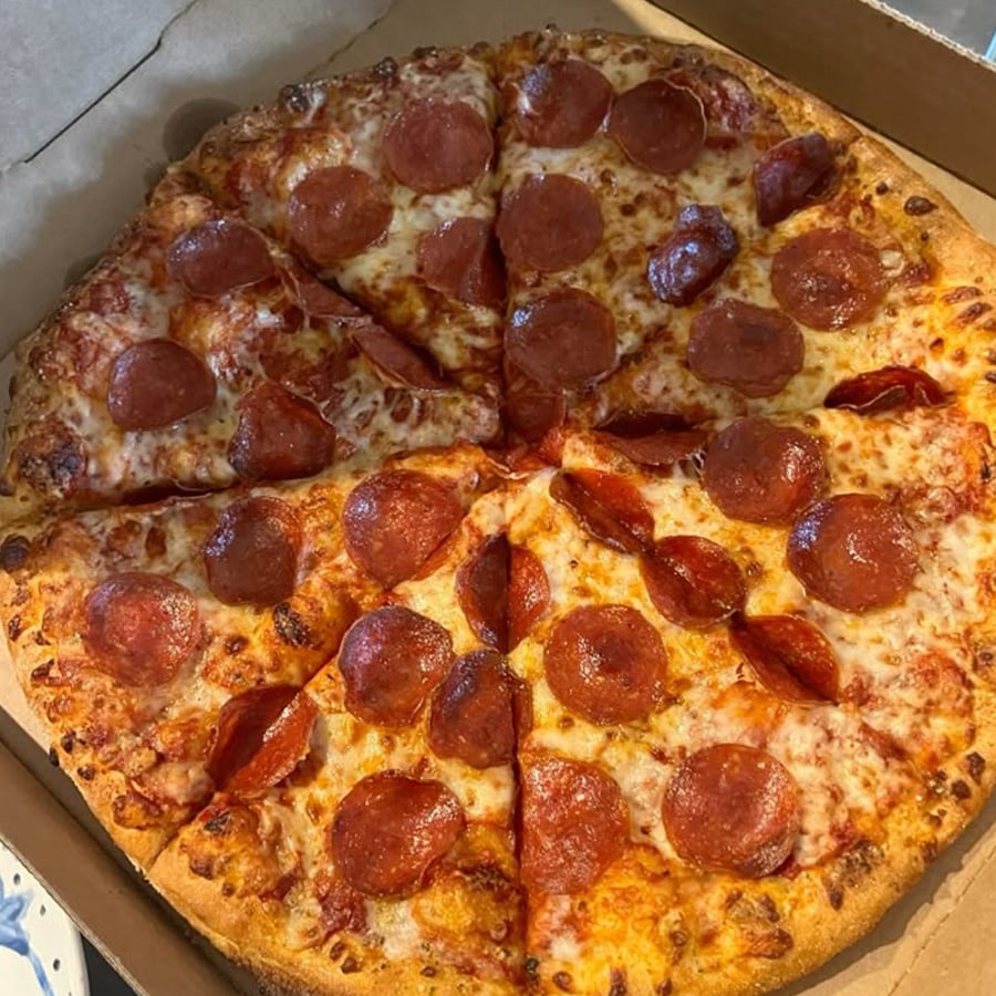 A pepperoni pizza with melted cheese and evenly spaced pepperoni slices, cut into eight pieces and served in an open cardboard box.