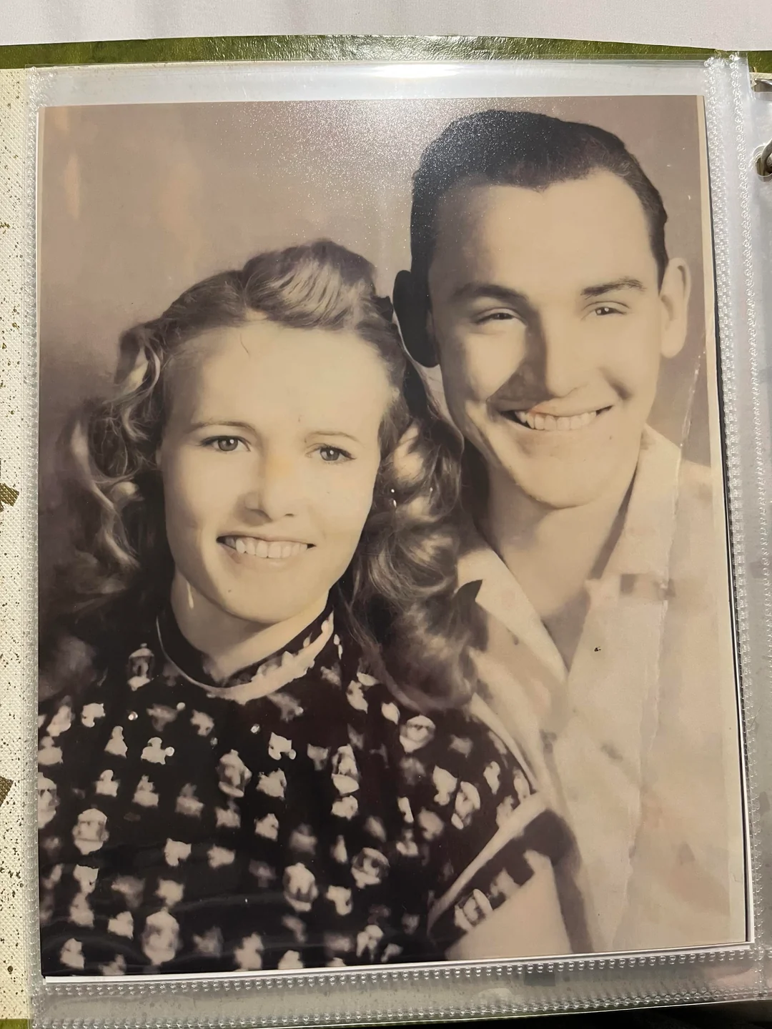 A vintage black and white photo of a smiling woman with wavy hair and a patterned dress, next to a smiling man in a collared shirt.