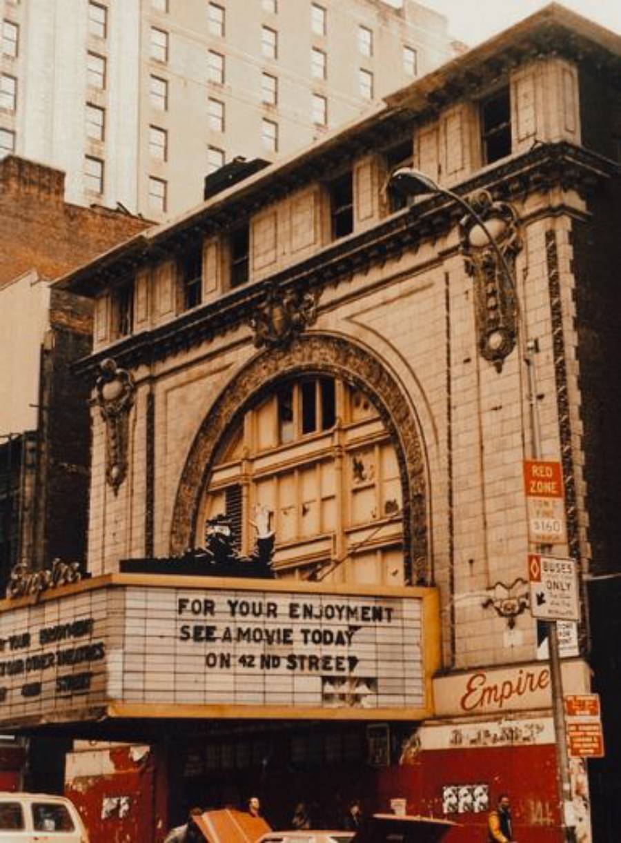 An old, ornate theater with a large arched facade and marquee sign reading “FOR YOUR ENJOYMENT SEE A MOVIE TODAY ON 42ND STREET.” The building appears weathered, with the word “Empire” visible below the sign.
