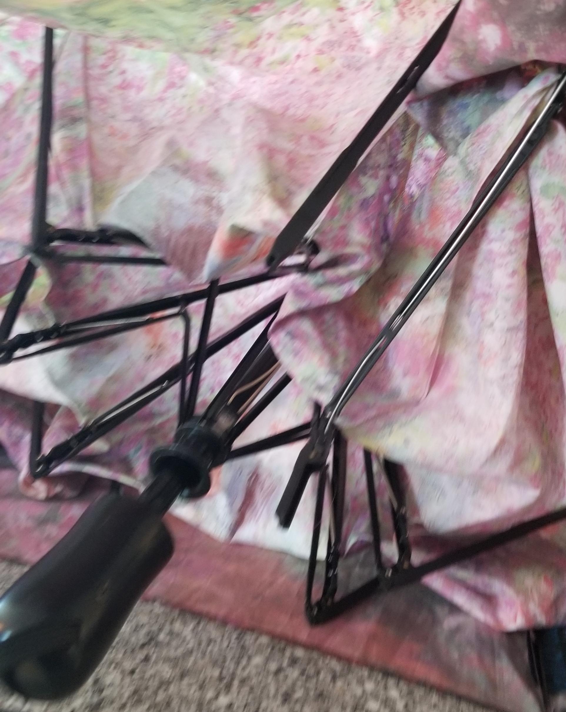 A close-up of a damaged floral-patterned umbrella with bent black metal spokes and a black handle, resting on a speckled surface.