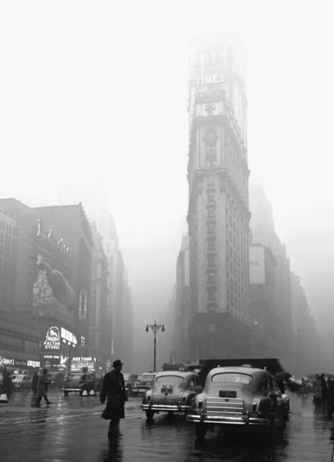 A foggy city street scene from the past with vintage cars, people walking, and a tall building with “TIMES” on its sign, partially obscured by mist.