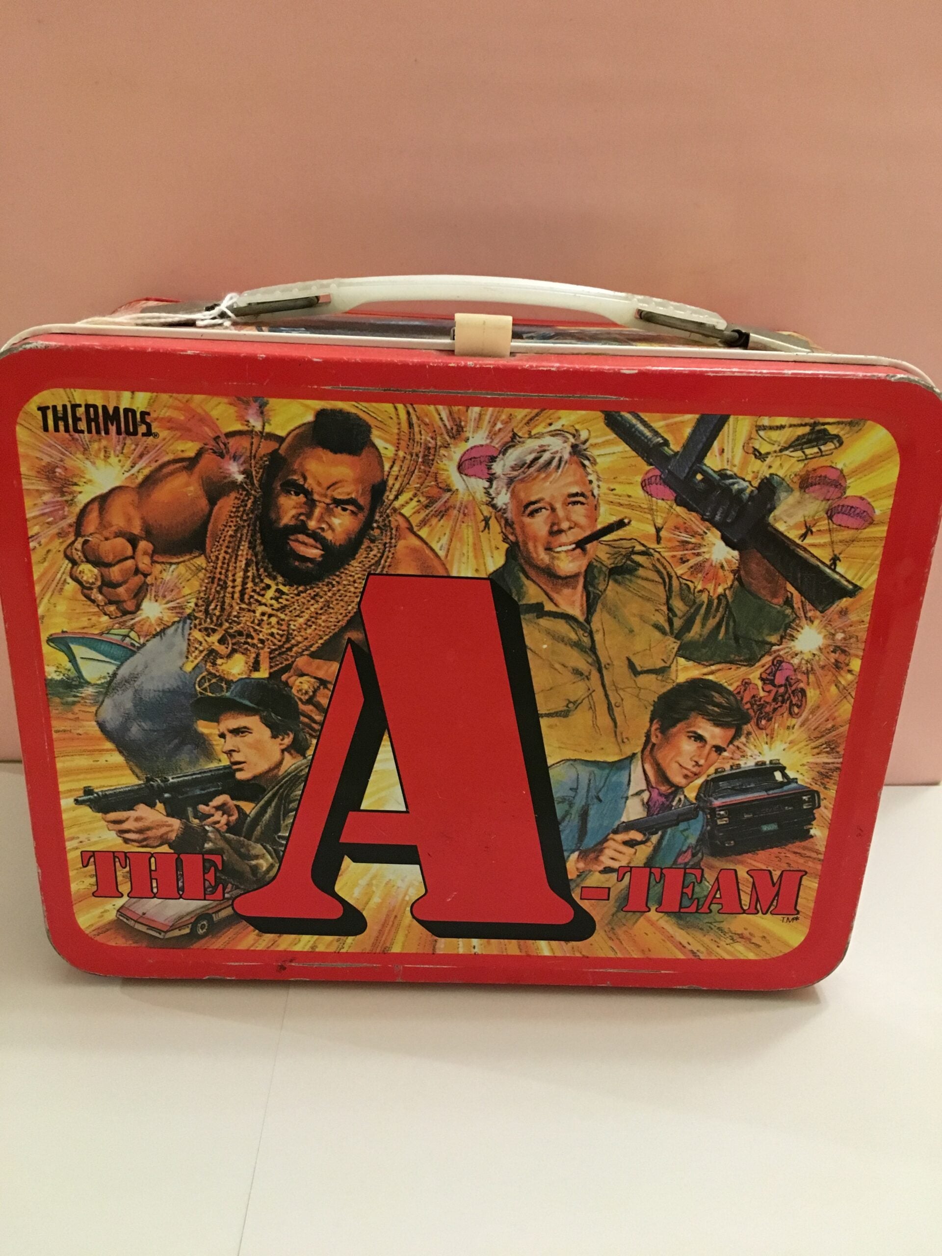 A red metal lunchbox featuring "The A-Team" characters, including Mr. T, surrounded by action scenes, cars, a helicopter, and a large red letter "A" in the center.