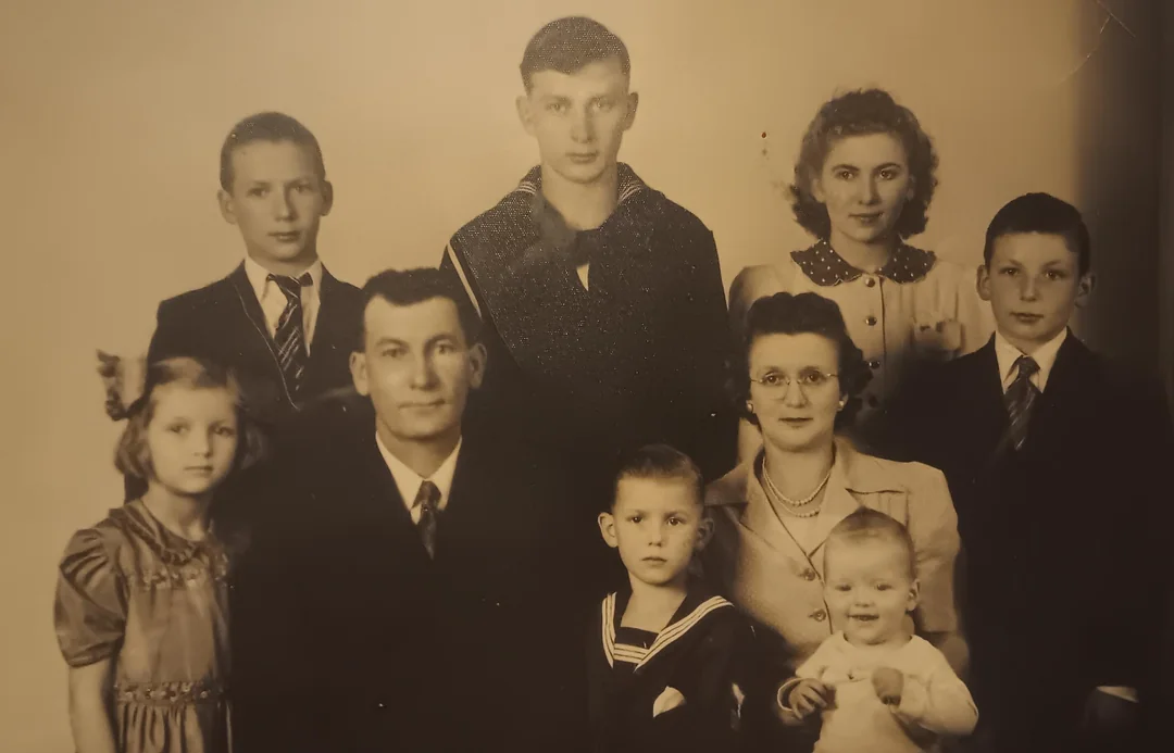 A vintage sepia-toned portrait of a family with five boys, one girl, an infant, a man, and a woman, all dressed formally and posing together, likely in the mid-20th century.