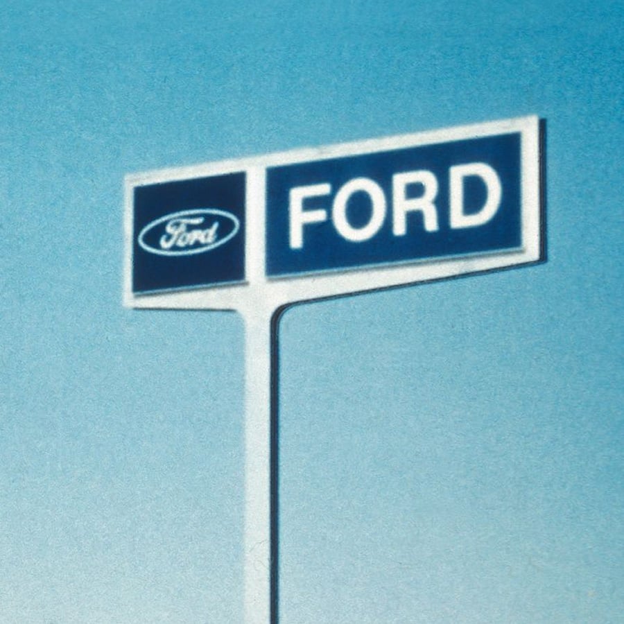 Tall sign with the Ford logo and the word "FORD" in white on a blue background, set against a clear blue sky.