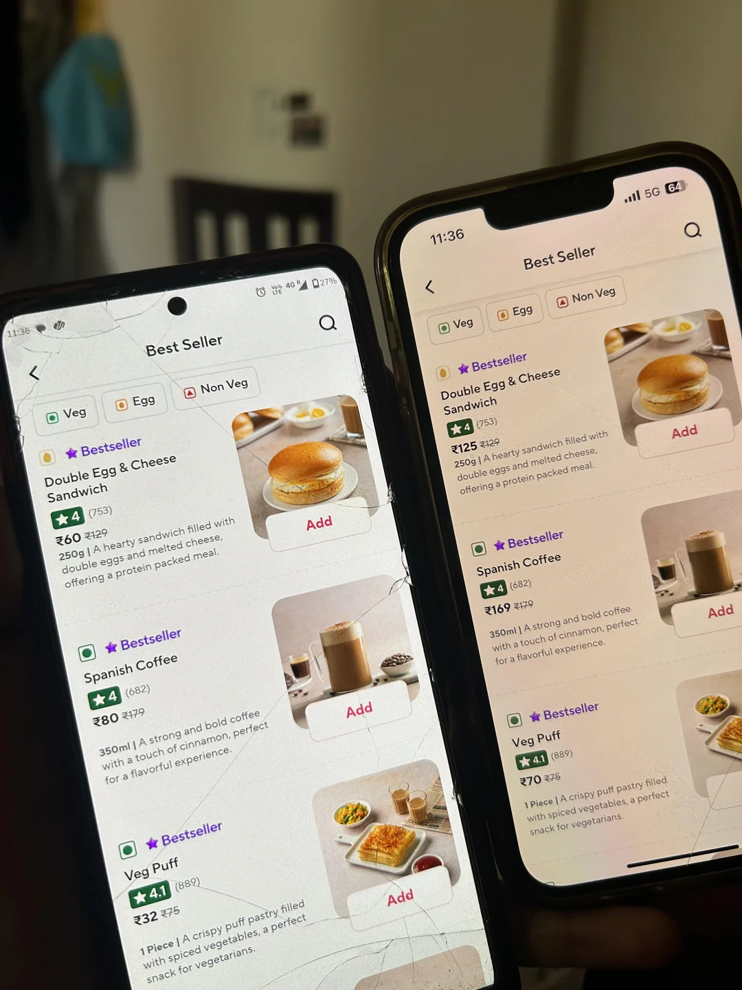 Two smartphones display the same food delivery app screen showing best-selling breakfast items like a double egg sandwich and coffee. Both phones have cracked screens and are angled side by side on a blurry indoor background.