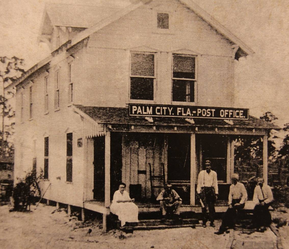 Historic black-and-white photo of five people sitting and standing on the porch of the Palm City, Fla. Post Office, a two-story wooden building.