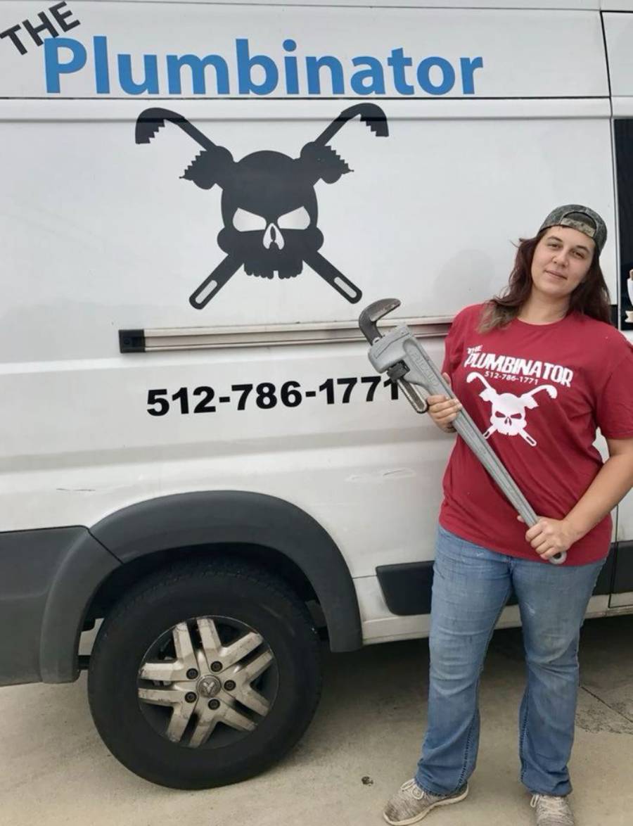 A woman in a red "The Plumbinator" shirt holds a large wrench and stands by a van with "The Plumbinator" logo, featuring a skull and crossed pipe wrenches.