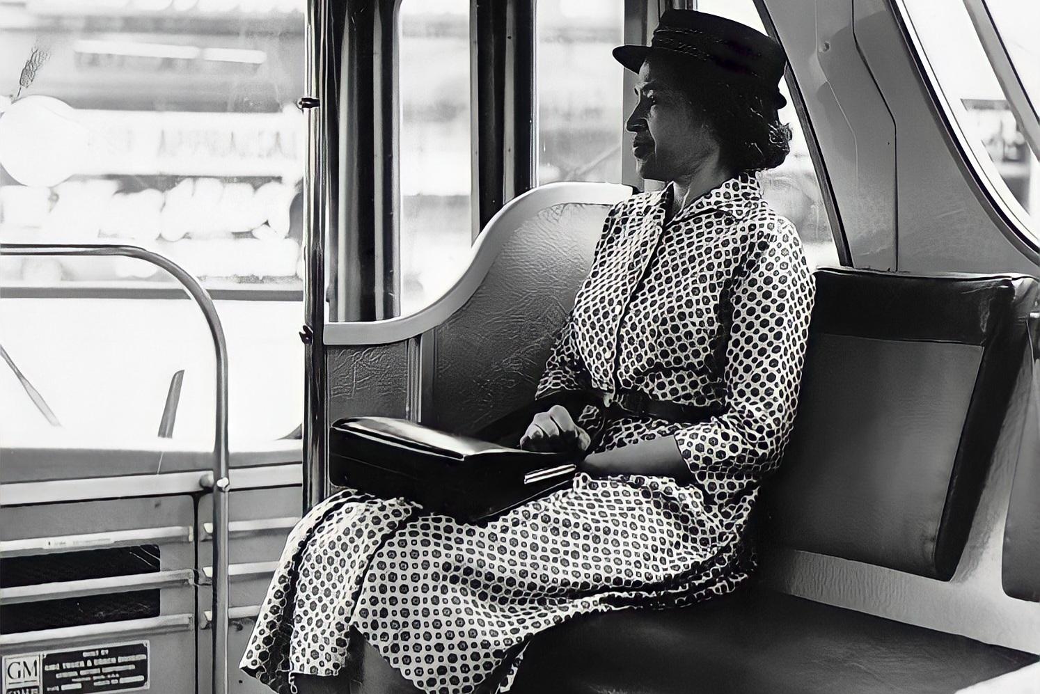 A woman in a patterned dress and hat sits alone on a bus, holding a handbag in her lap, gazing out the window in a thoughtful manner.