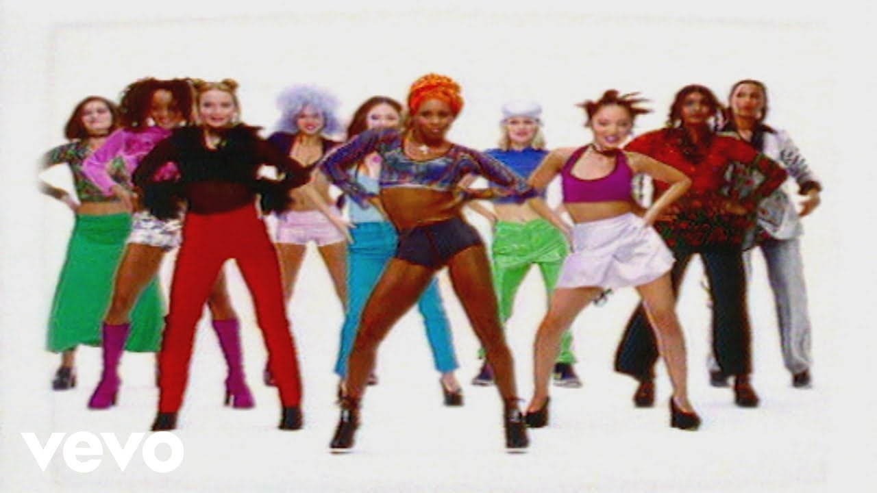A group of diverse women in colorful, 90s-inspired outfits pose confidently against a white background, with some smiling and hands on hips.