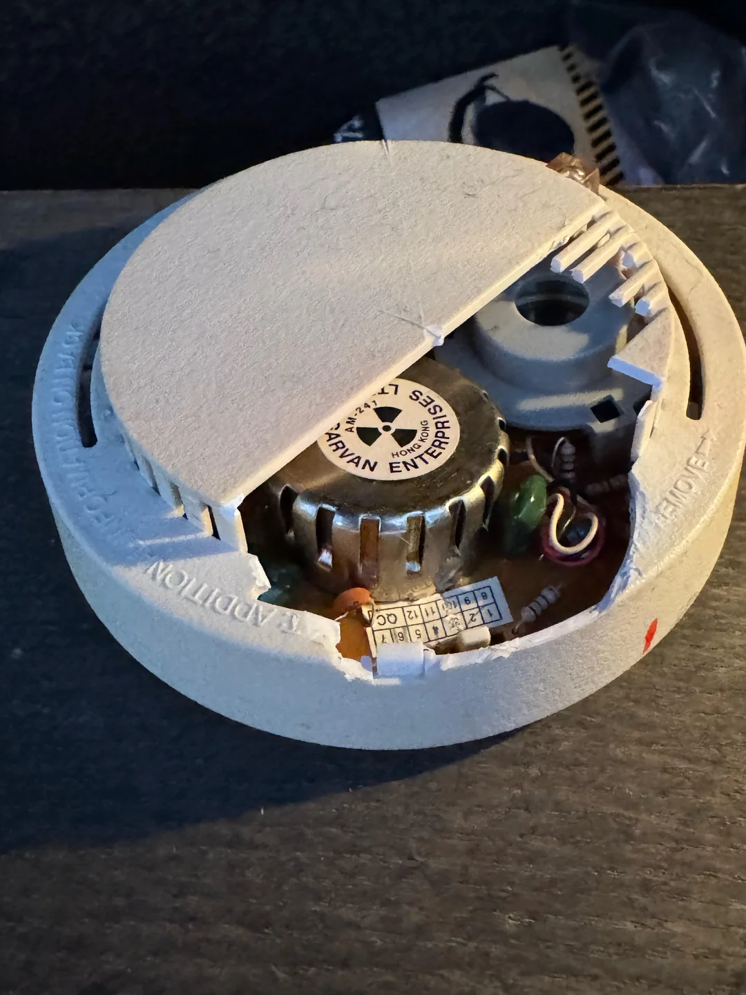 A close-up of a smoke detector with its cover partially removed, revealing inner electronic components and wiring inside the device.