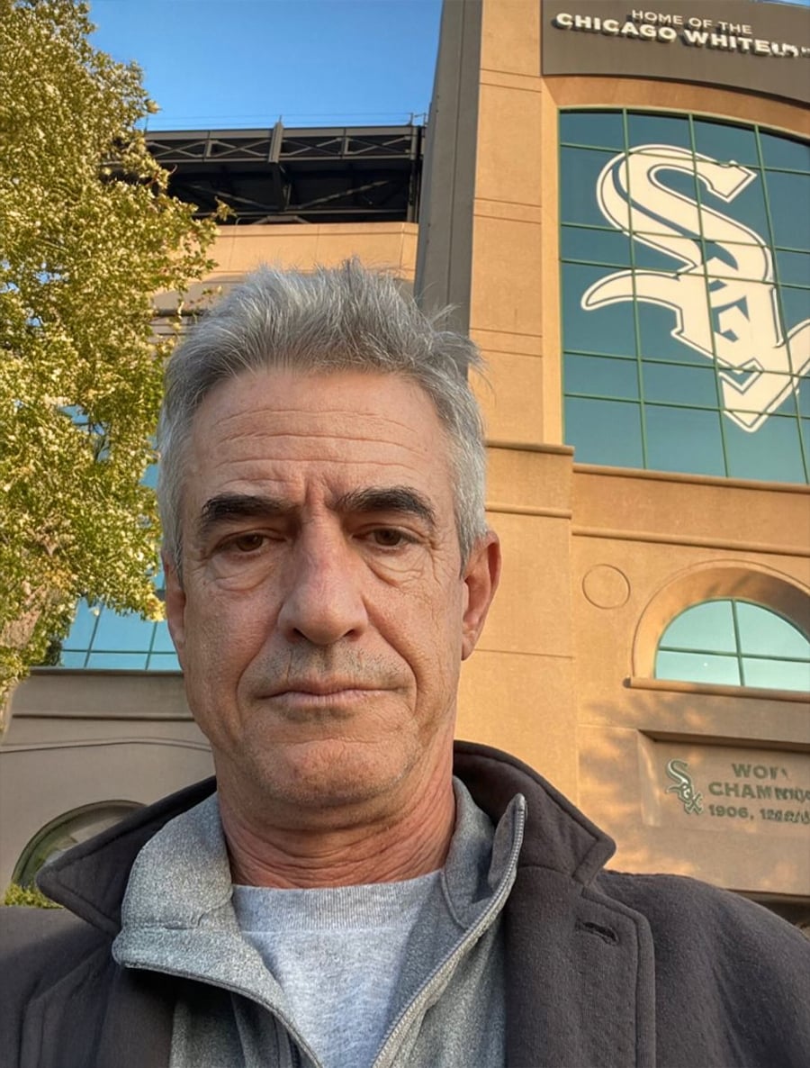 A man with gray hair stands outside of Guaranteed Rate Field, home of the Chicago White Sox, with the stadium logo and signage visible behind him on the building.