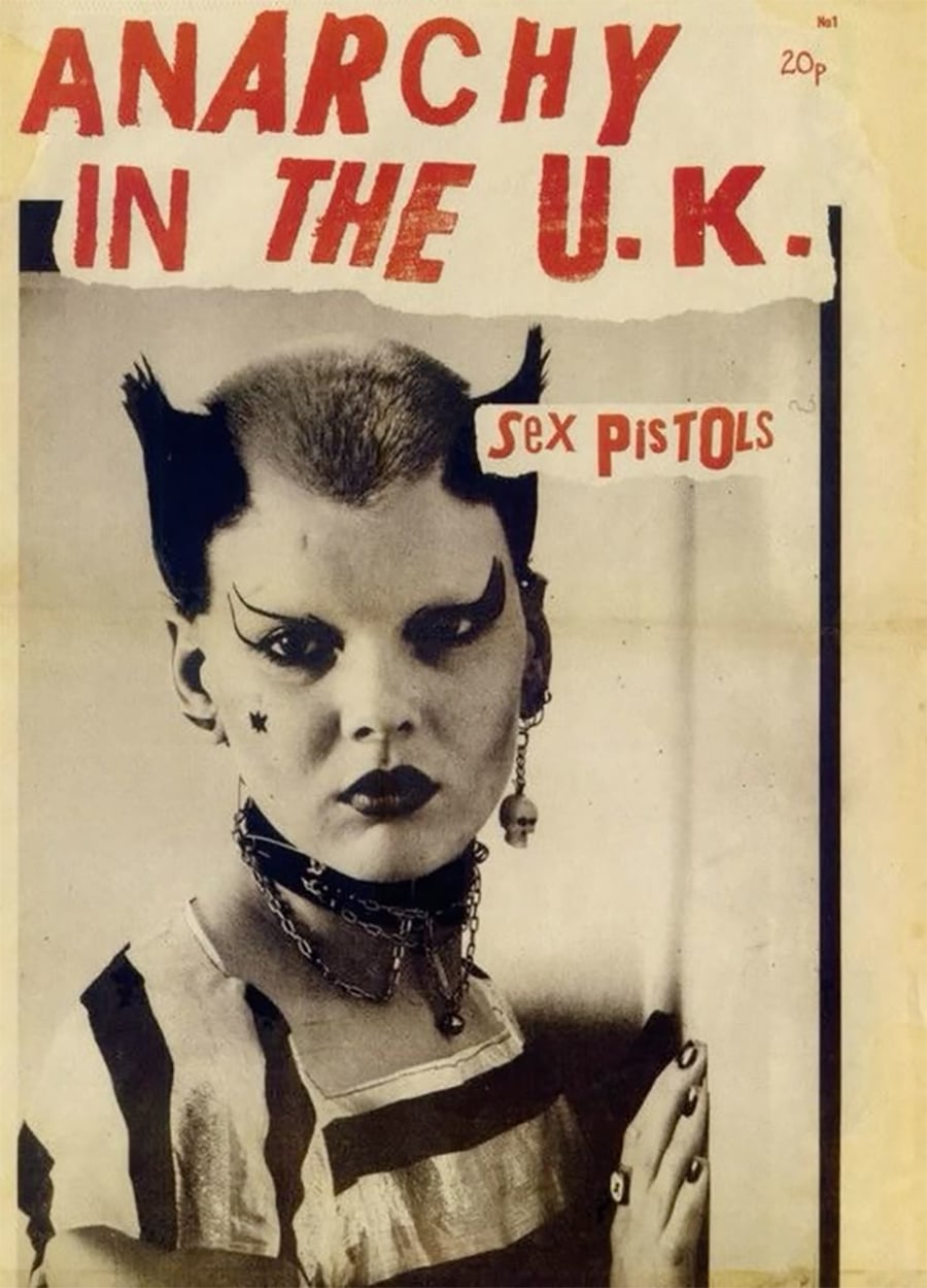A punk-styled person with dramatic makeup, spiked hair, chained necklace, and striped shirt appears on a vintage poster reading "ANARCHY IN THE U.K. Sex Pistols" in bold red and black text.