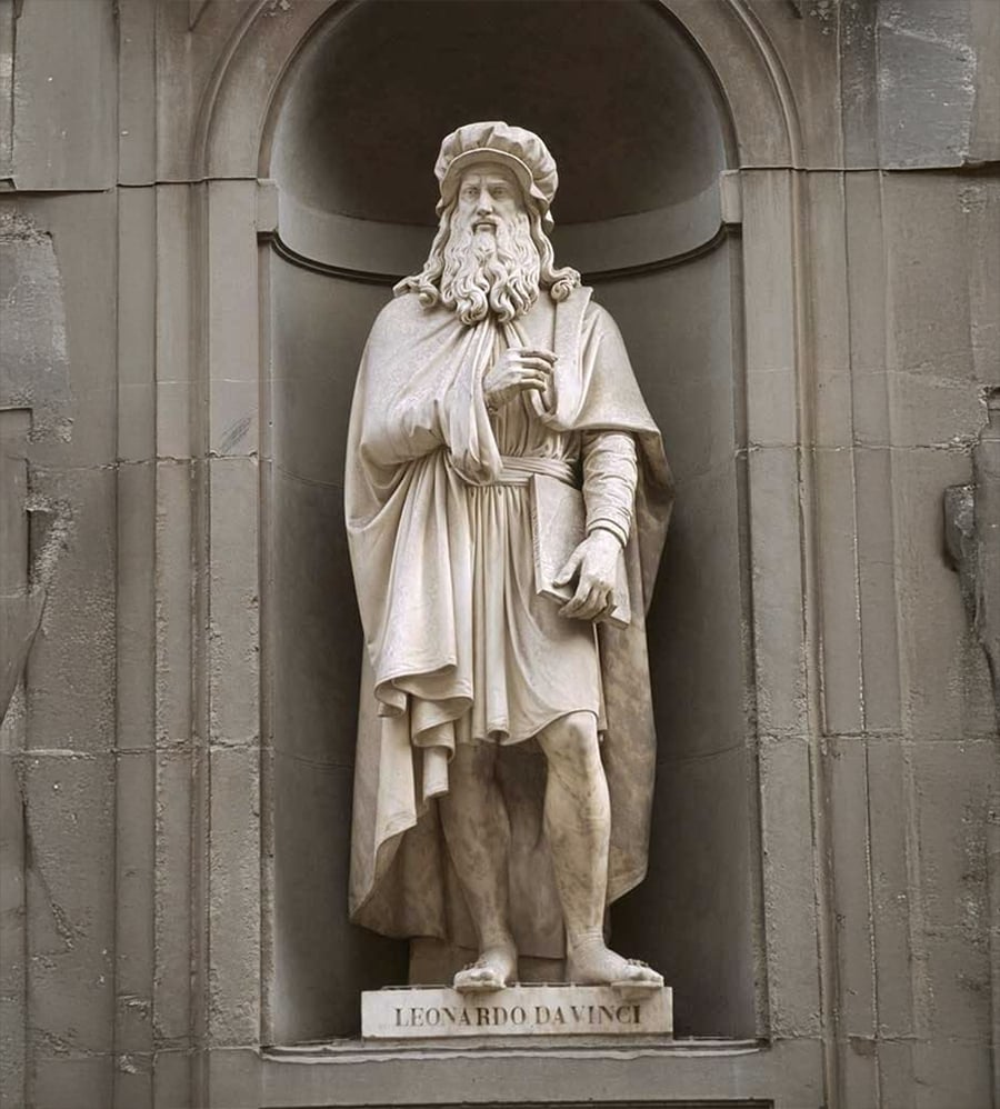 Statue of a bearded man in Renaissance attire, standing in an arched niche. The base of the statue is inscribed with "Leonardo da Vinci.