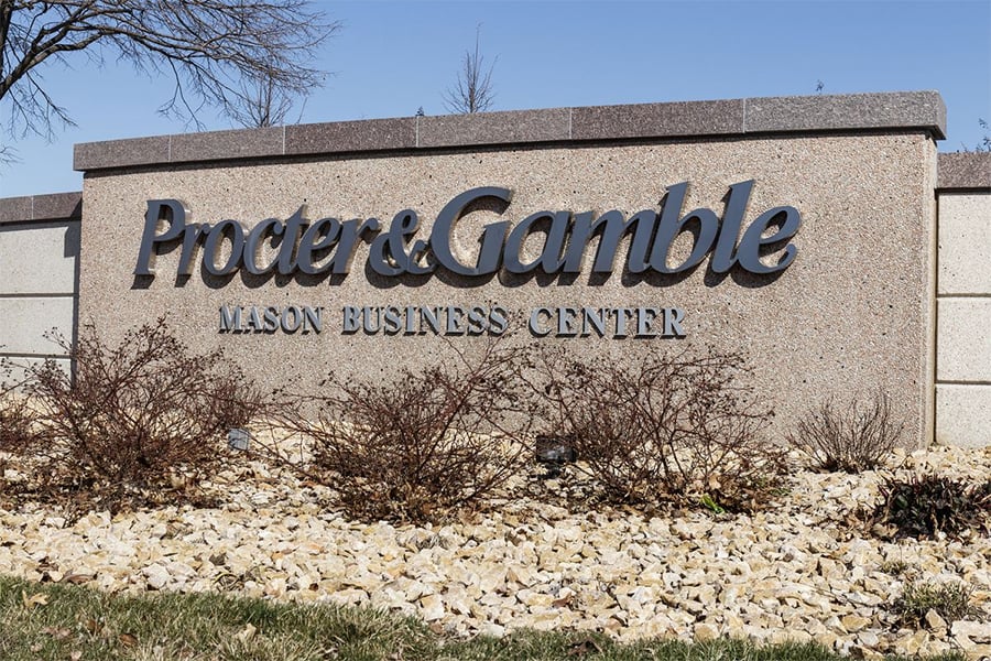 A stone sign reads "Procter & Gamble Mason Business Center" with bushes and rocks in front and a clear sky in the background.