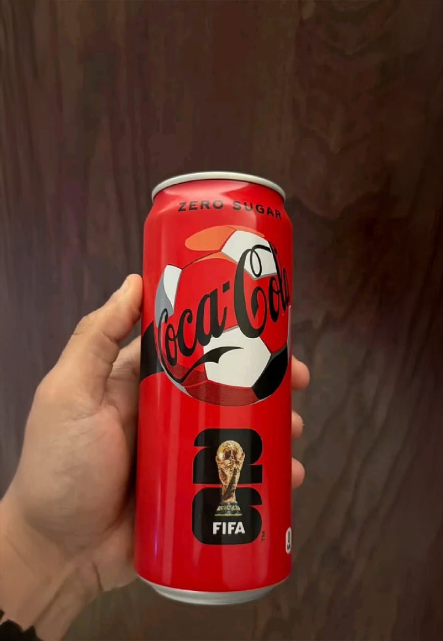A hand holds a red Coca-Cola Zero Sugar can featuring a soccer ball design and the 2026 FIFA World Cup trophy logo on the front.
