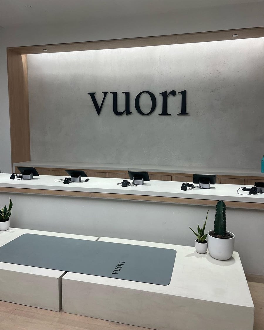 A modern retail counter with "vuori" on the wall, several checkout stations, and potted plants on white counters.