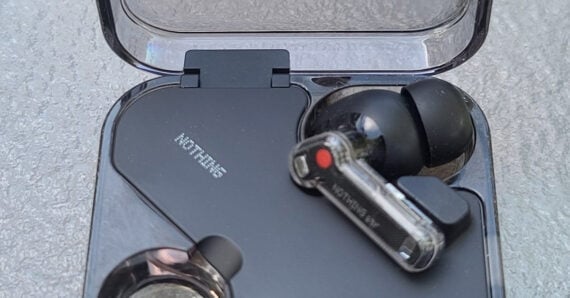 A close-up of a pair of black wireless earbuds in a transparent charging case, showing the "NOTHING" brand name on both the case and one earbud.