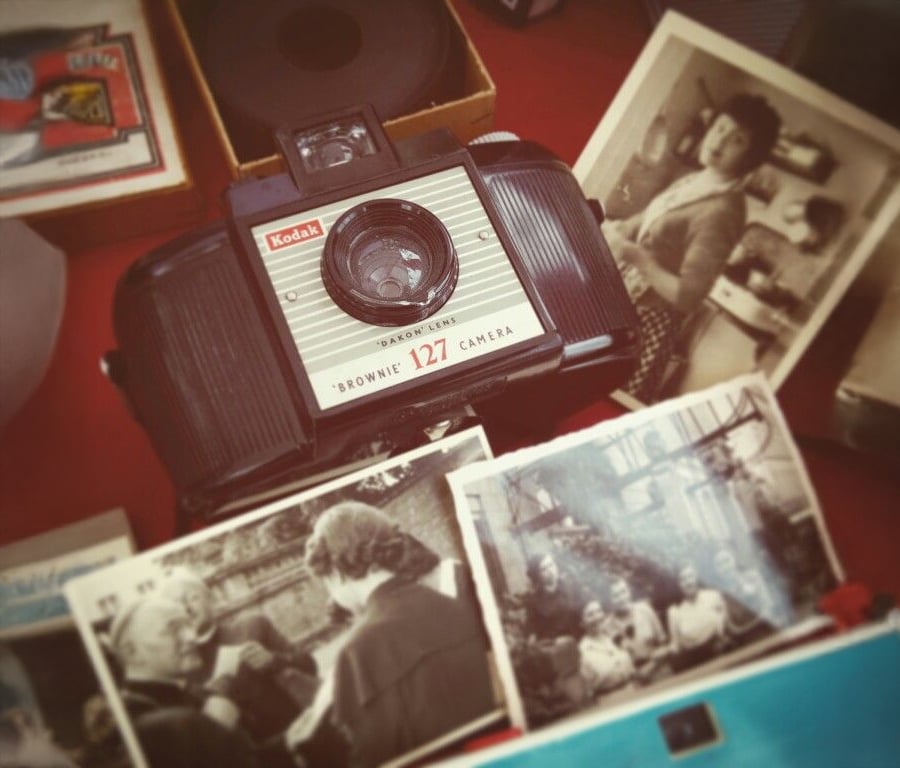 A vintage Kodak Brownie 127 camera sits on a table surrounded by black-and-white family photographs and a few boxes, creating a nostalgic atmosphere.