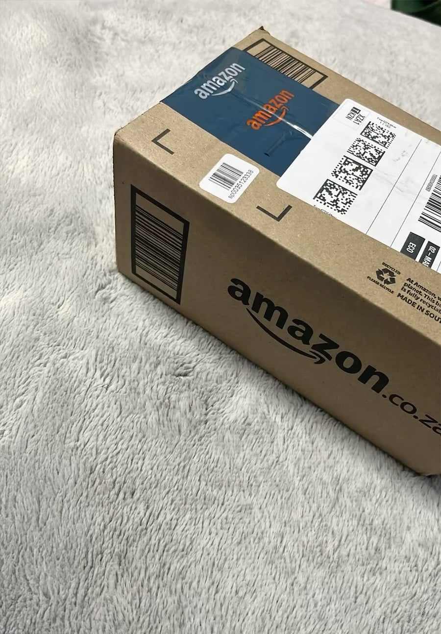A brown Amazon.co.za package with a barcode and shipping label sits on a soft, light gray textured surface.