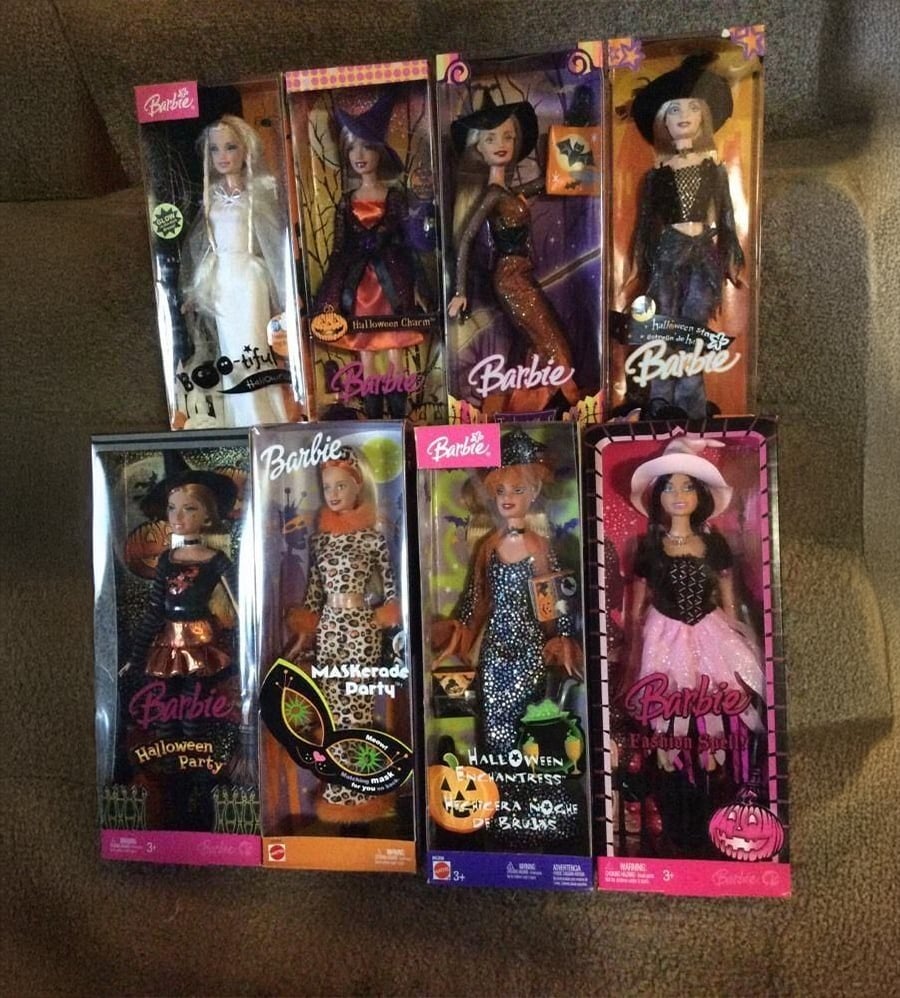 Eight Halloween-themed Barbie dolls in boxes are arranged on carpeted stairs. Each doll wears a different costume, including witches, a leopard, and a ghost, with colorful packaging featuring festive graphics.