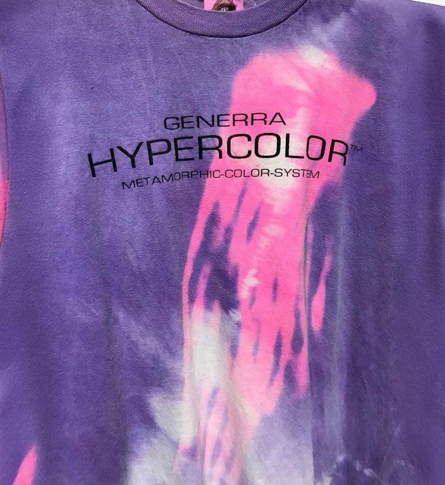 Close-up of a purple and pink Genarra Hypercolor shirt with black text reading, “GENERRA HYPERCOLOR METAMORPHIC-COLOR-SYSTEM,” and abstract color patterns on the fabric.