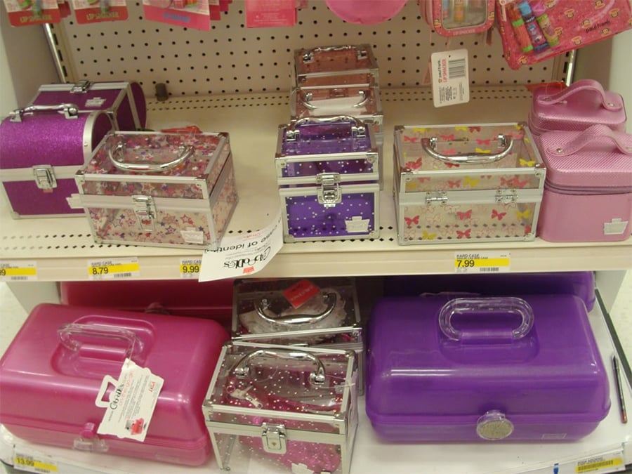 Small, colorful, rectangular vanity and storage cases, some glittery and floral, displayed on white store shelves with price tags attached.