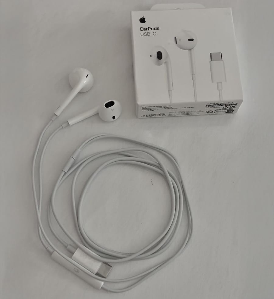 A pair of white Apple EarPods with a USB-C connector is coiled next to its packaging box, which shows an image of the earphones and the text “EarPods USB-C.”