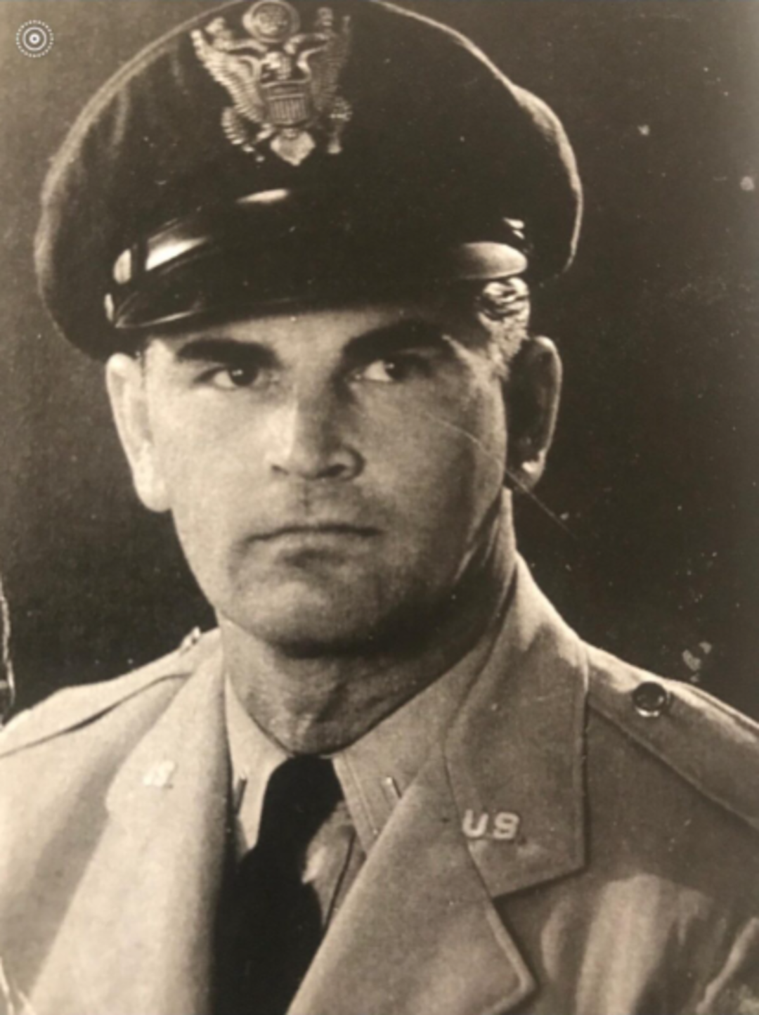 Black-and-white photo of a man in a U.S. military uniform and cap, facing slightly to the left. The cap has an insignia, and "U.S." pins are visible on his collar. He has a serious expression.