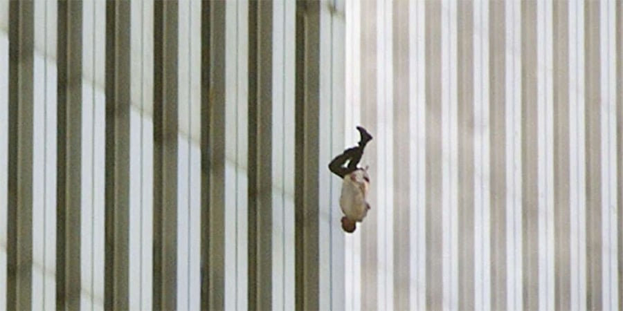 A person falls headfirst from a tall building with vertical striped glass windows, wearing a white shirt and dark pants. The background shows repeating lines of the facade.