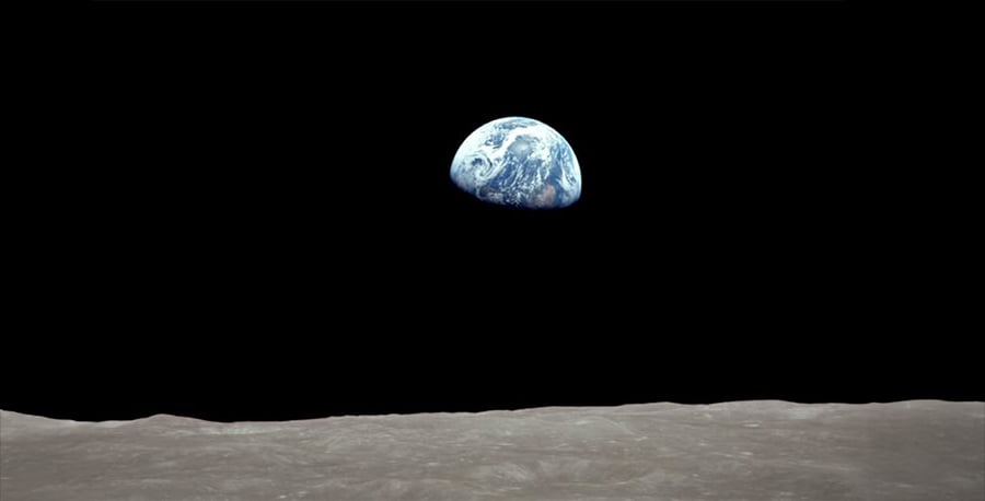 View of Earth rising above the Moon's barren horizon, with the planet appearing blue and white against the blackness of space.