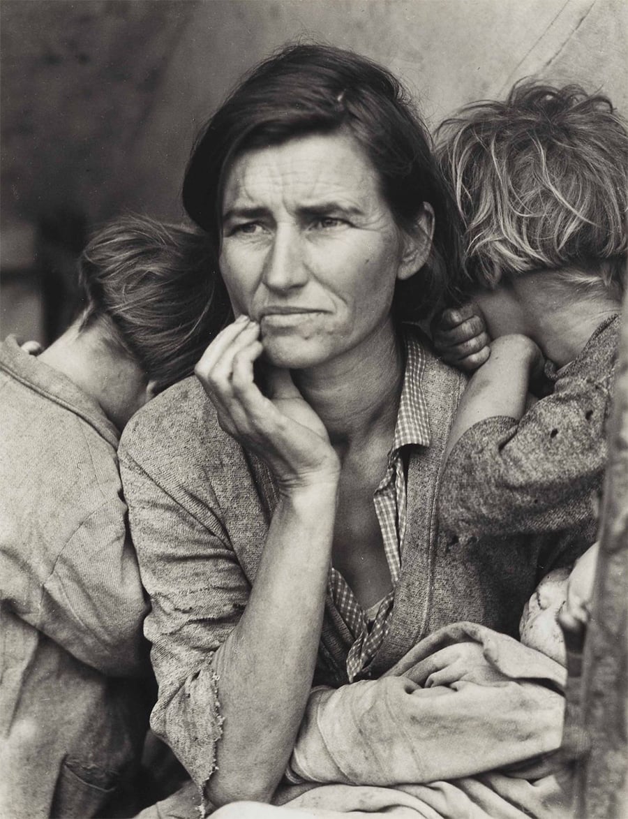 A woman with a worried expression sits with her hand on her face, two children leaning on her shoulders, their faces turned away. The black-and-white photo captures a somber, reflective moment.