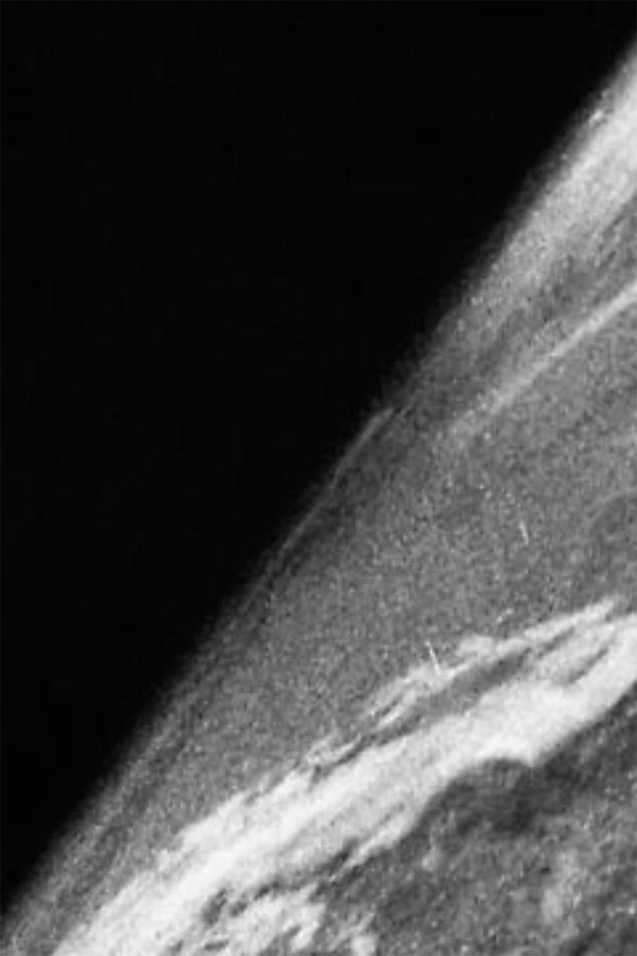 A black-and-white image of Earth's curved surface seen from space, with cloud formations visible, and the dark expanse of outer space in the background.