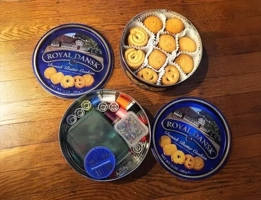 Three Royal Dansk Danish butter cookie tins: one open with cookies, one open with sewing supplies, and one closed, all placed on a wooden floor.