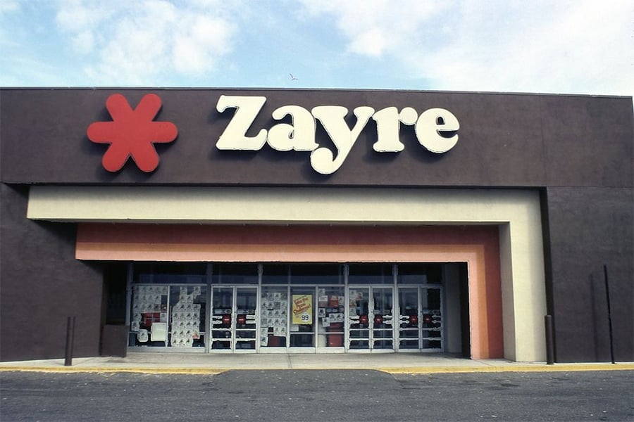The front of a Zayre store with large white letters and a red asterisk logo above the entrance. The building is brown with glass doors and product displays visible inside.
