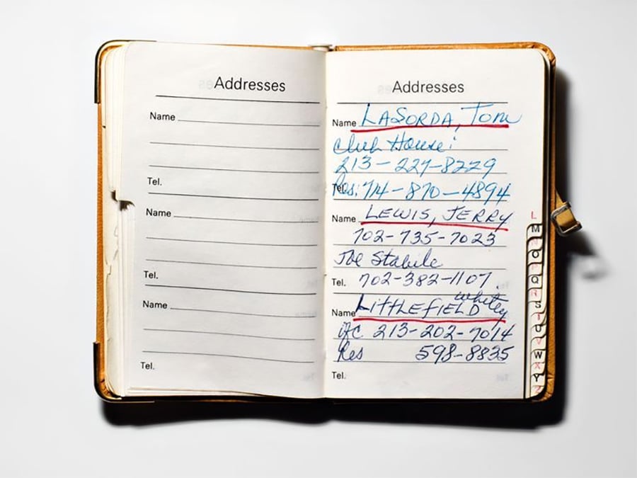 An open address book showing handwritten contact information for several people, including names, addresses, and phone numbers, written in blue and black ink on lined pages.