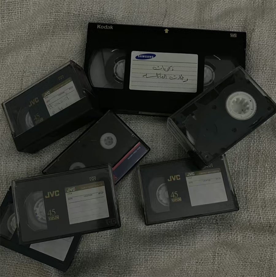 A group of VHS and JVC cassette tapes scattered on a textured beige fabric surface, with handwritten labels visible on some tapes.