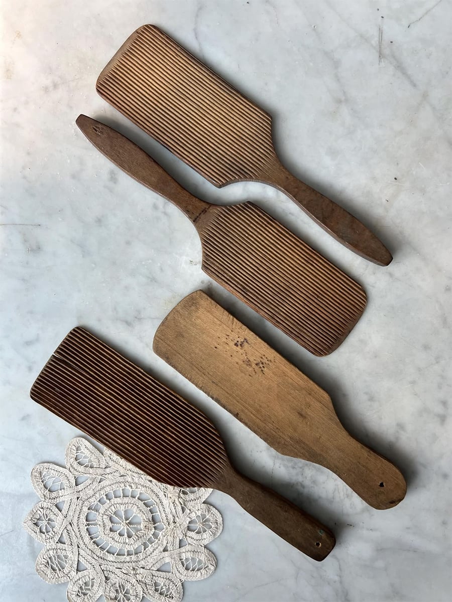 Four vintage wooden butter paddles with grooved surfaces lie on a marble surface, next to a small piece of white lace.