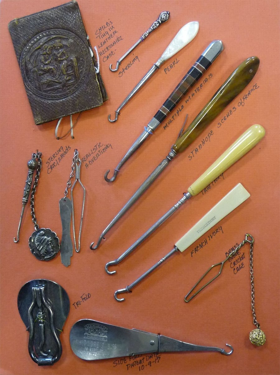 A collection of antique buttonhooks and related accessories, displayed on an orange background, each labeled by material and type. Items include various handled hooks, a notebook, and metal shoehorns.