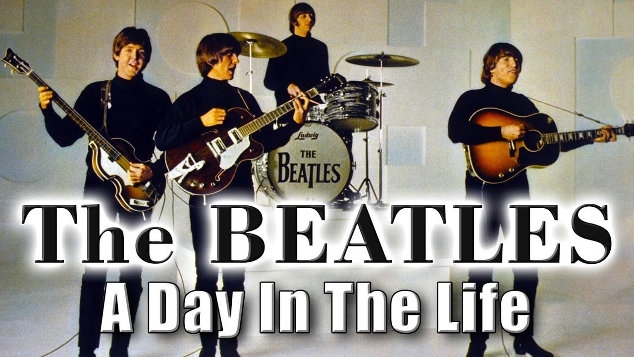 Four men in black outfits play guitars and drums on stage. The drum set reads “The Beatles.” Bold text says “The BEATLES A Day In The Life.” The background is light-colored with circular patterns.