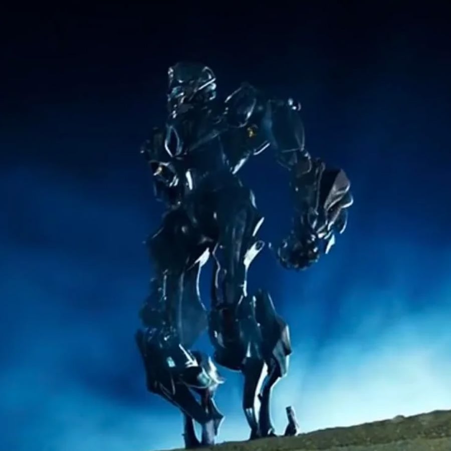 A large, metallic robot stands on a hill at night, illuminated by a blue glow, with clouds or mist in the background and a small human figure at its feet.