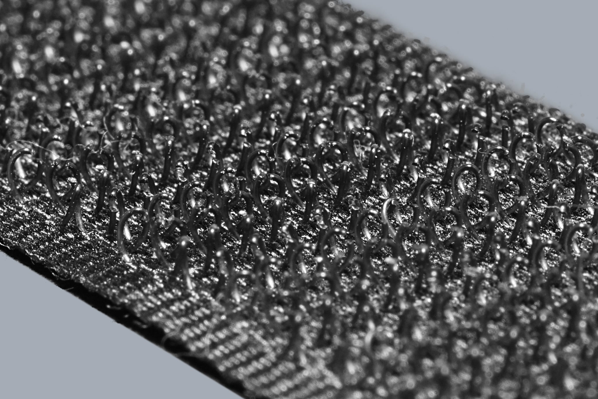 Close-up image of the hook side of a fastener strip, showing many tiny, curved plastic hooks used for attaching to the loop side, commonly known as Velcro.