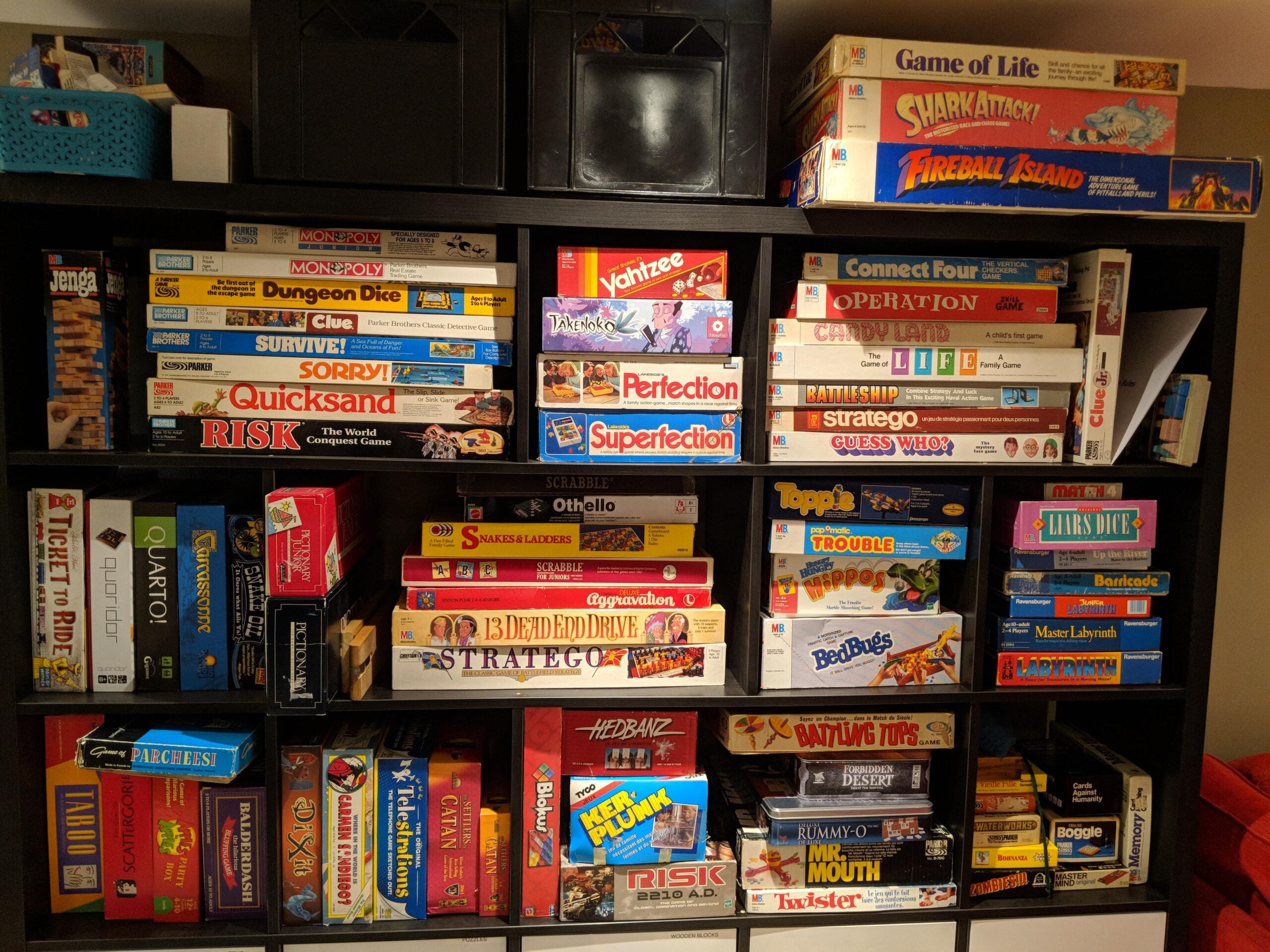 A black bookshelf filled with various board games, including Life, Risk, Jenga, Operation, Sorry!, Stratego, and others, all stacked closely together.