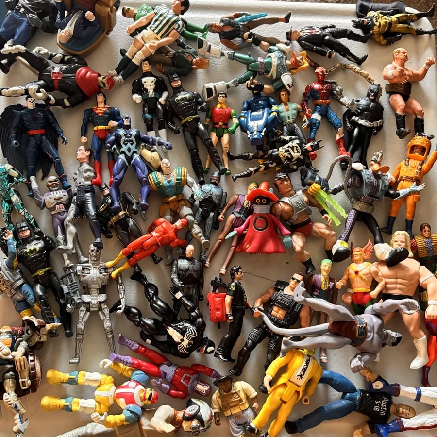 A collection of assorted action figures, including superheroes, robots, and wrestlers, is scattered randomly across a flat surface.