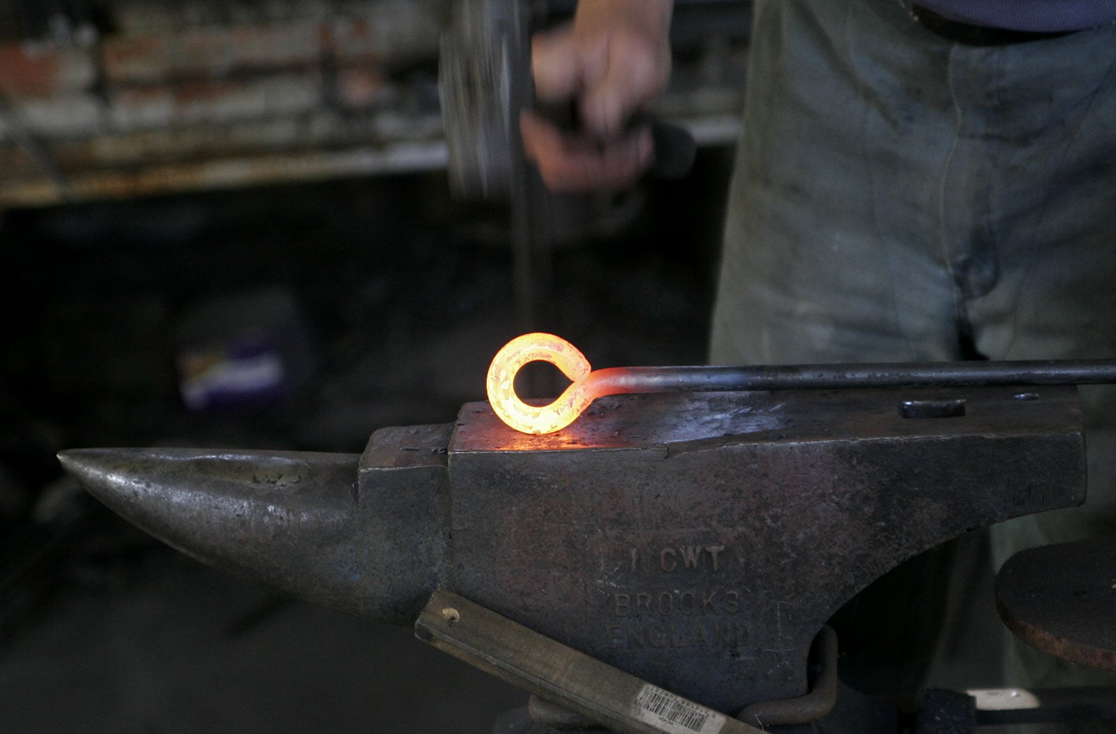 A person uses a hammer to shape a glowing hot metal ring on an anvil in a workshop.