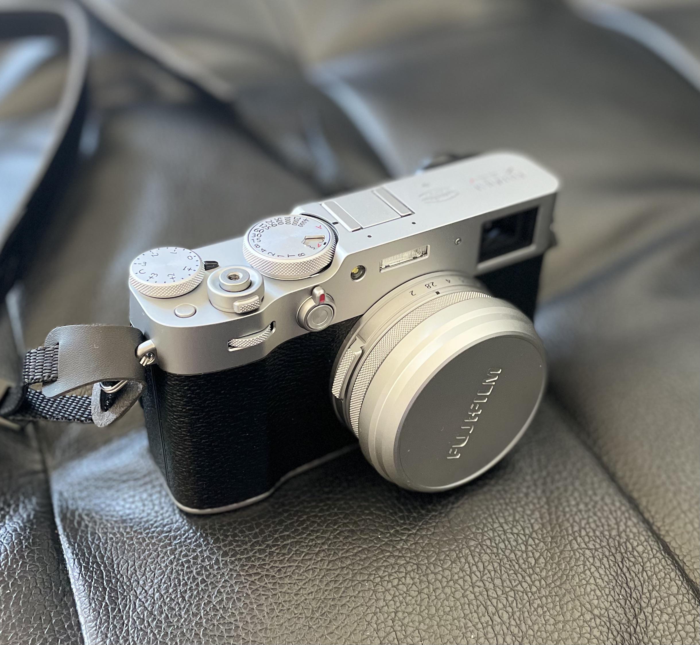 A silver and black Fujifilm camera with a lens cap rests on a textured black leather surface.