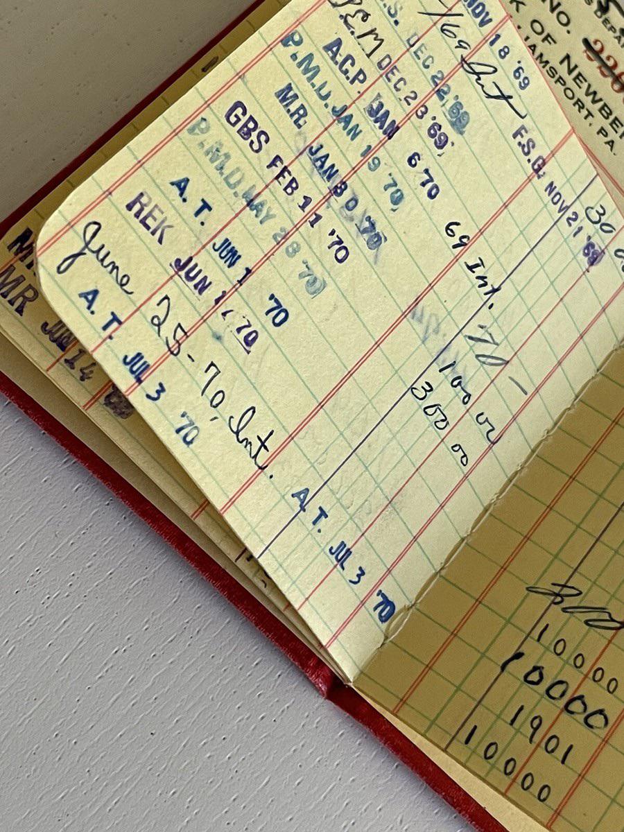 An old, yellowed library checkout card in a red sleeve, showing handwritten dates and initials from 1970. The card is partially open, revealing multiple columns and stamps.