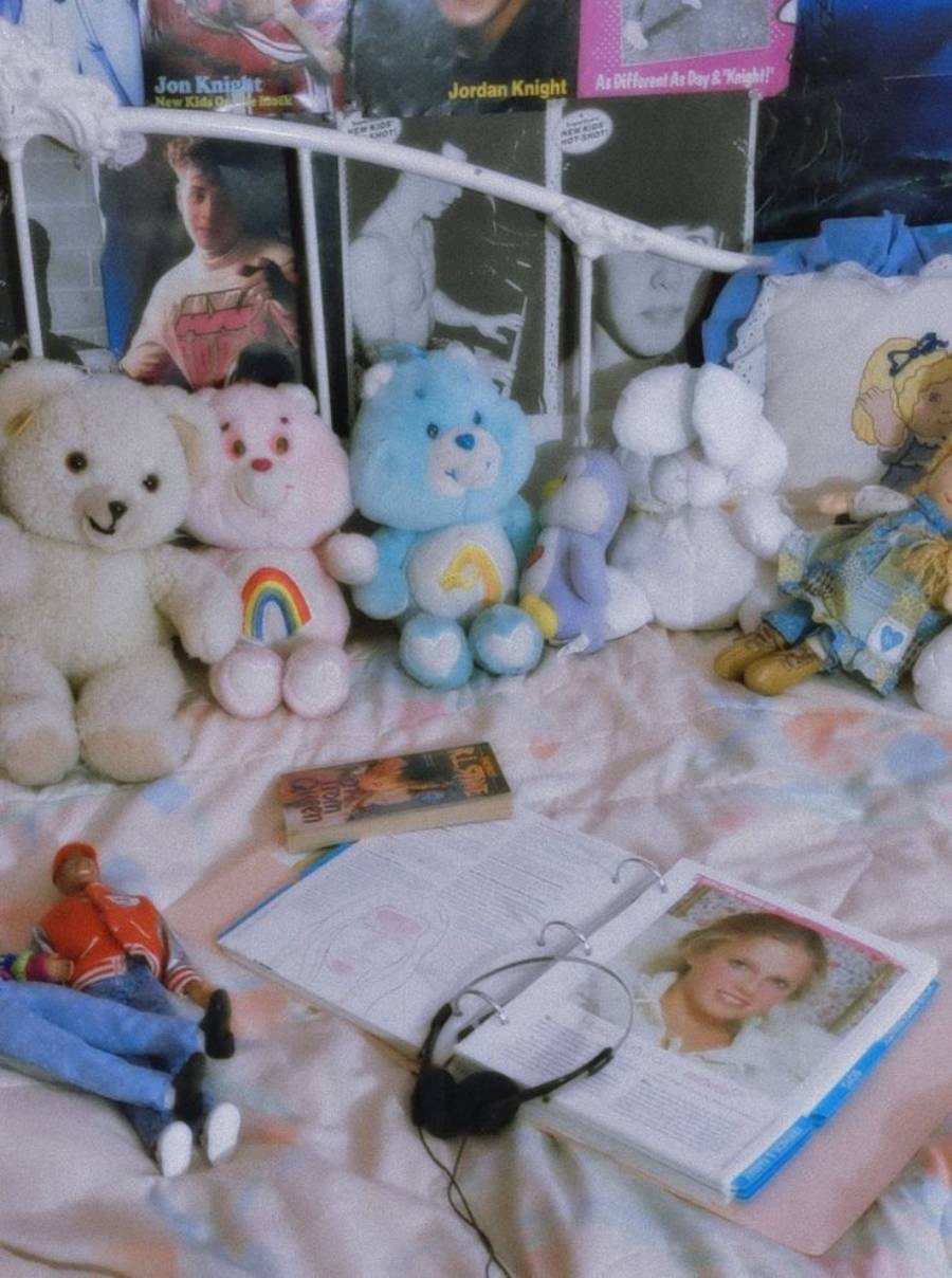 A bed with plush teddy bears, a doll, a cassette tape, headphones, an open magazine, and posters of singers on the wall in a nostalgic, colorful bedroom setting.