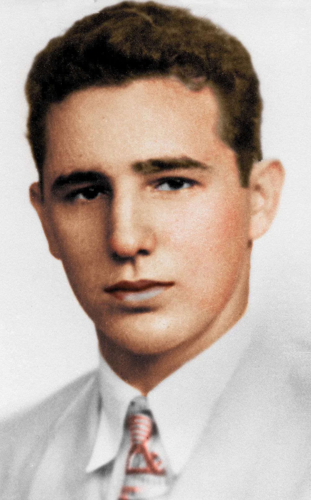 A young man with short brown hair wears a white collared shirt and striped tie, looking straight at the camera with a neutral expression against a plain background.