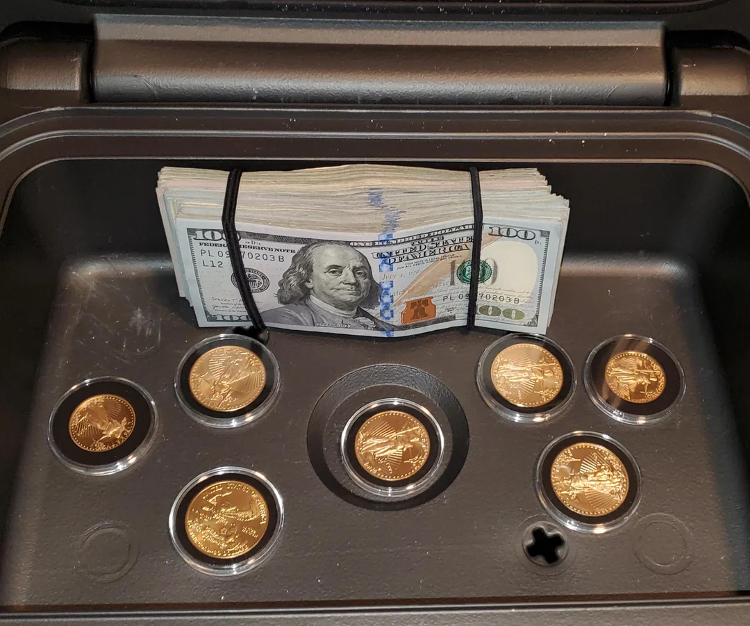 A stack of $100 bills secured with rubber bands sits in a safe, along with six gold coins in protective cases arranged in a circular pattern.